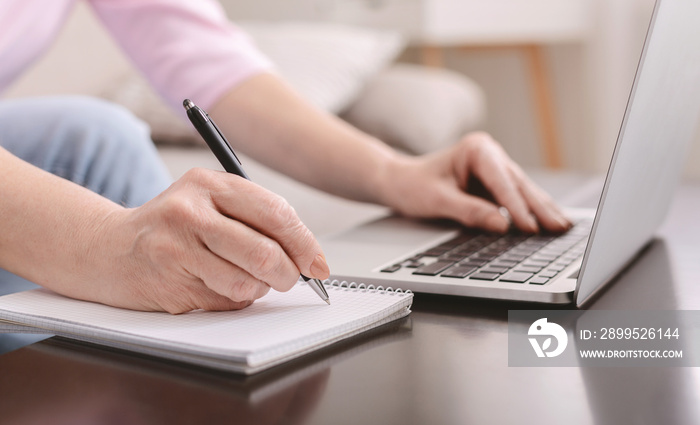 Senior woman writing down thoughts and working on laptop