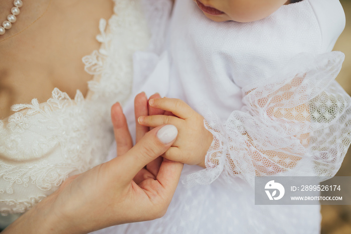 Close-up photo of a bride in wedding dress holding child hand on her wedding day. Wedding concept. Cropped shot.