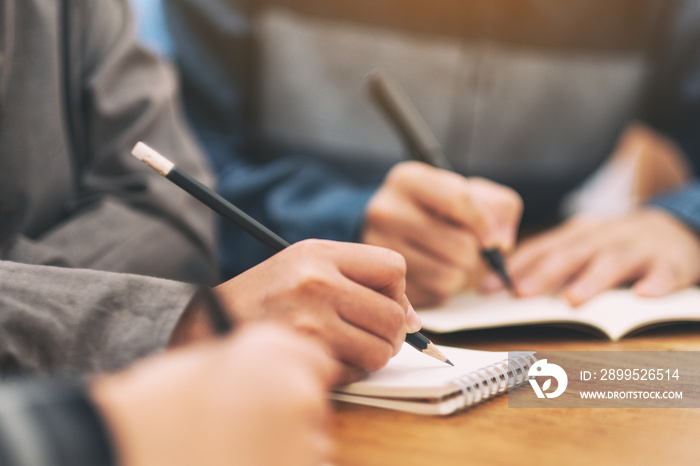 Closeup image of many people writing on blank notebook together on wooden table