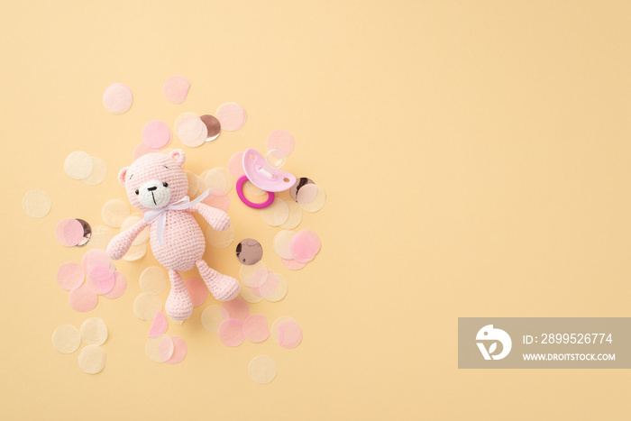 Baby accessories concept. Top view photo of pink knitted teddy-bear toy soother and shiny confetti on isolated pastel beige background