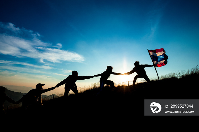 Leader handing Thailand Flag and climbers help A Team to conquer the summit in teamwork in a fantastic mountain landscape at sunset. Helping hand concept and international day of peace and teamwork.