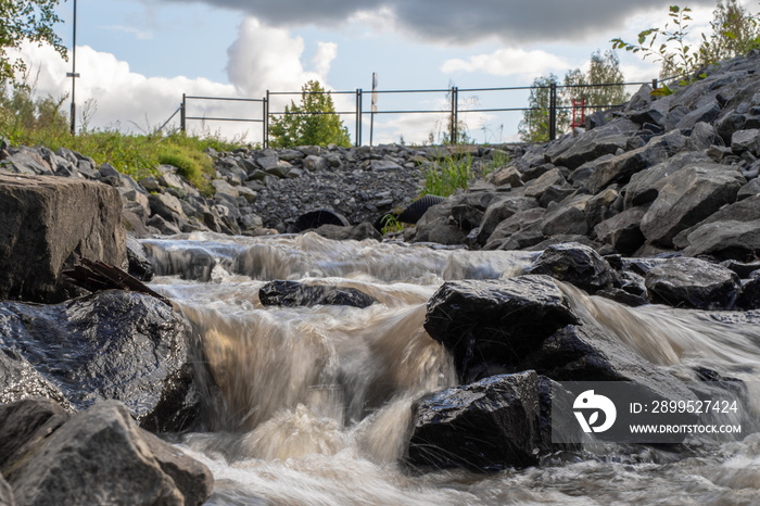 Loimijoki river in small Finnish city Forssa on a cloudy summer day. Flowing water over rocks, motion blur.