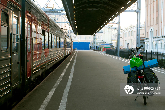 A bicycle with tourist equipment on the station feather. The train is preparing to leave. Tourist and solo travel concept. Road trip, staycations and back to basics idea.