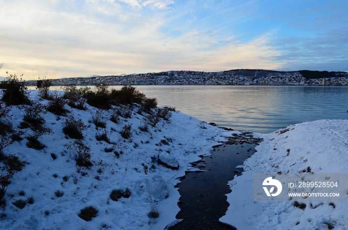 small creek stream in winter with the arctic circle city of Tromsoe in the background