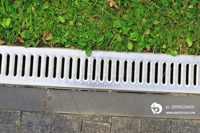 Drainage system separates the grass and the paved sidewalk. Sewerage and grate on the ground for water drainage