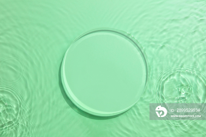 Empty Glass circle podium on transparent clear green water texture with splashes and waves in sunlight. Abstract nature background for product presentation. Flat lay cosmetic mockup.