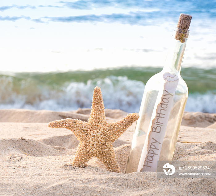 close up of starfish and happy birthday message in a bottle on the seashore with water background