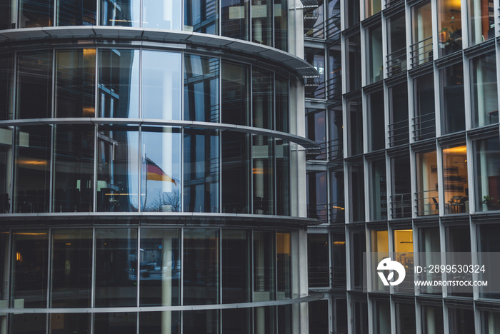 German flag reflected in governmental building. People working in the office building in the evening. Modern architecture in Berlin, German Chancellery