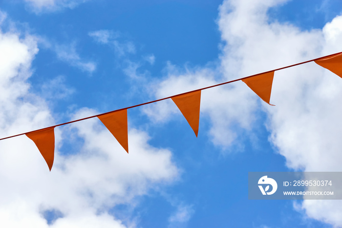 A row of orange triangle pennant banner flags on Koningsdag. A national holiday in the Netherlands against a blue sky with clouds and copy space