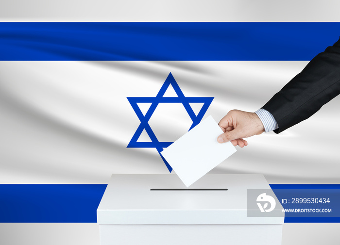 Election in Israel. The hand of man putting his vote in the ballot box. Waved Israel flag on background.