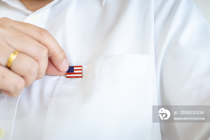 Close up of man hand holding United State of America nation flag pin on white shirt flag.