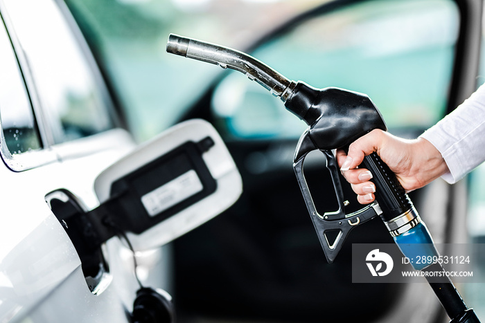 Woman pumping petrol at gas station into vehicle. Hand holding a pistol or nozzle pump prepare to refuel car with gasoline.