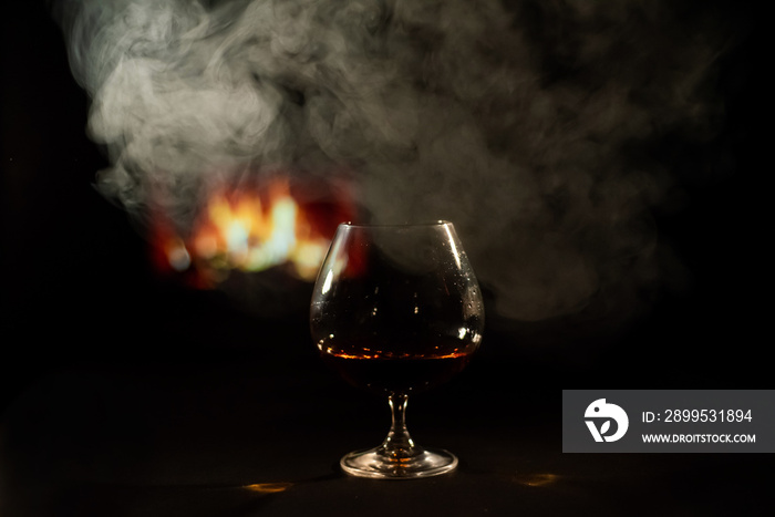 A glass of brandy and cigar smoke in the dark on the background of the fireplace. Gentlemen’s club concept