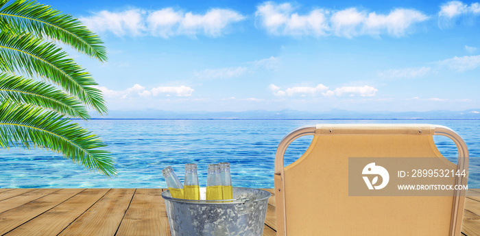 Refreshment drink of four beer bottle in bucket on wooden terrace and blue sea and palm leaf