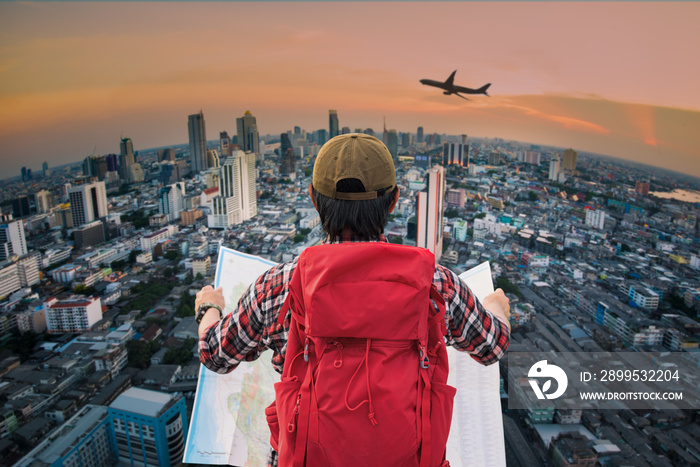 Young man wanderer holding a map and searching direction on location map and look to the city top view with searching direction in a map while traveling abroad. Tourist searching location concept