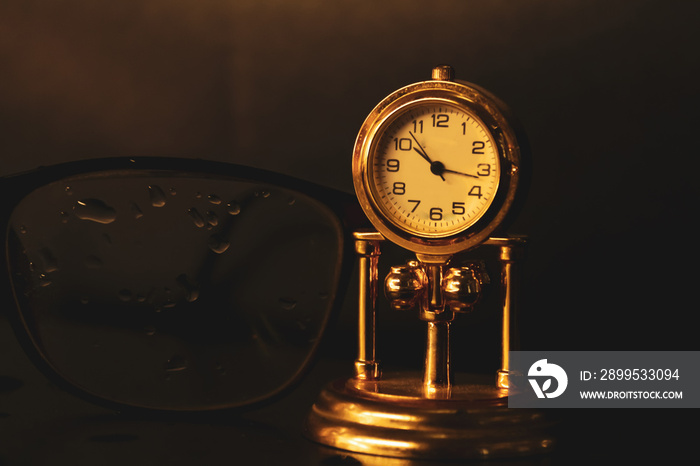 old clock and reading glasses on black background