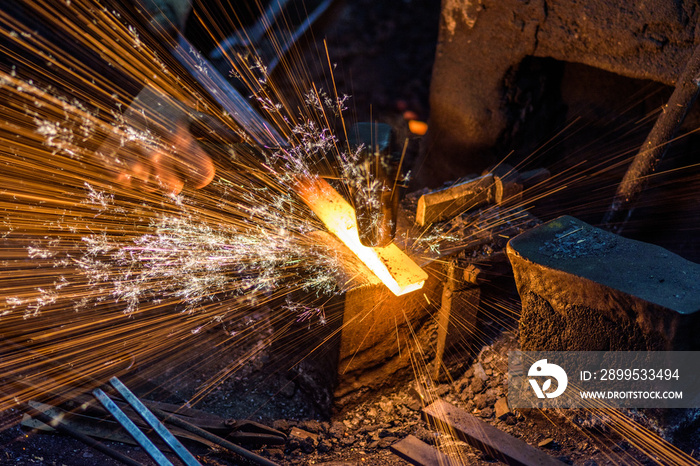 Blacksmith forging the molten metal on the anvil with spark fireworks