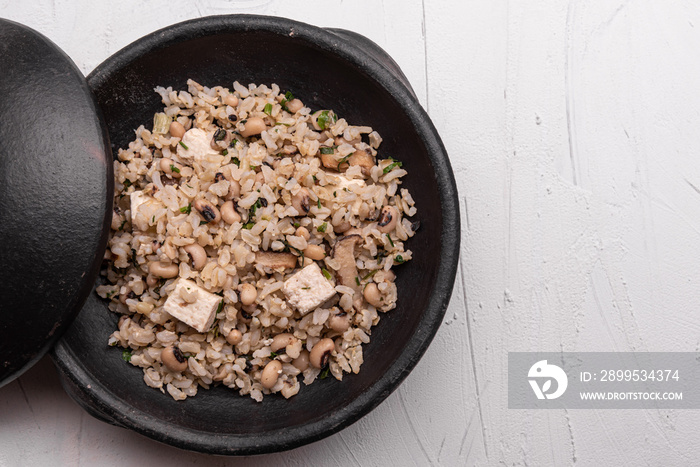 Baião de Dois - Brazilian Traditional Food - made with sausage, curd cheese, dried beef and rice in a black clay pot, on white background. Typical dish of Northeast Brazil.