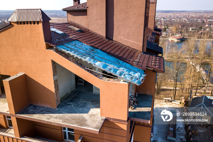 Aerial top view of unfinished tall apartment building, annex room under construction, high chimneys and plastic windows on tiled roof.