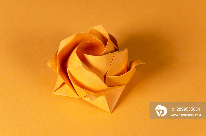 Orange origami rose on orange background. Japanese art of paper folding. Flat square sheet of paper transferred into a finished sculpture through folding and sculpting. Close up. Macro photo.