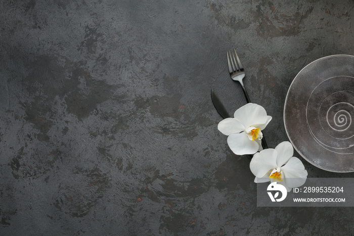 Elegance table setting with knitted grey napkin, cutlery, ceramic plates, glasses and white orchid flowers