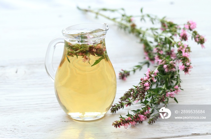 Herbal tea in glass with fresh flowers of hyssopus, lat. Hyssopus officinalis. Homemade tea from hyssopus and hot water in a jug on white wooden table.