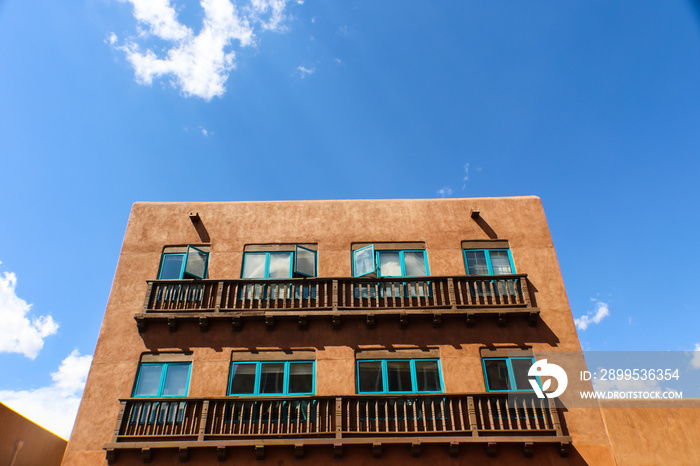 Santa Fe adobe Building with balconies and turquoise windows against a blue sky with clouds