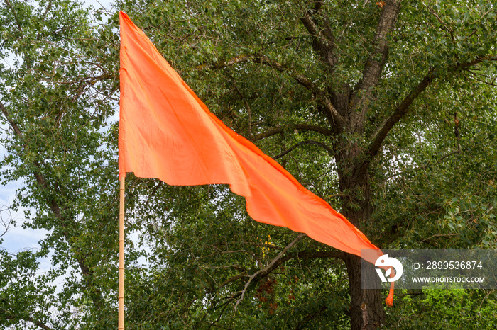 Orange flag flutters in the wind against the background of the trees.