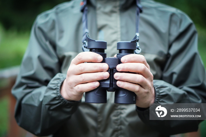 Close up of a man dressed in a hunter jacket holds binoculars in his hand.