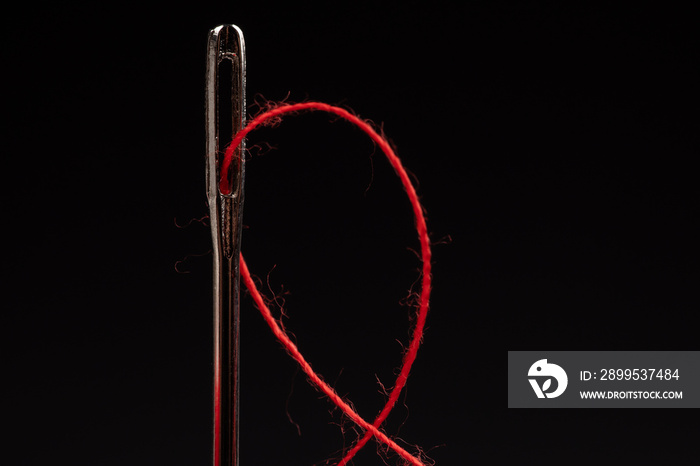 Red thread and needle on black background