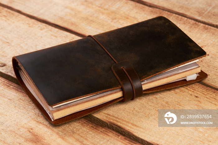 Old vintage leather book on wooden background. Handmade paper diary notebook in brown leather cover