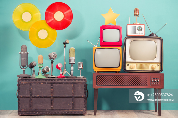 Retro studio microphones, outdated TV set, old FM radio, golden award star,  flying multicolor LP vinyl record discs front blue background. Nostalgia music and journalism concept. Vintage style photo