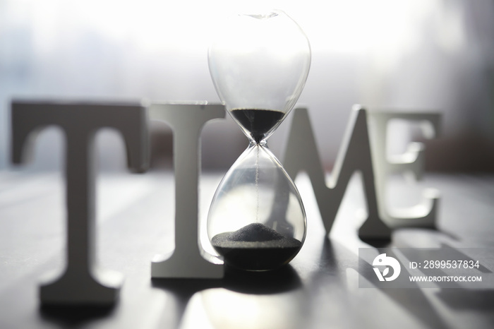 The concept of the passage of time. Hourglass on a dark background. Inscription time. The shadow on the surface of the word.