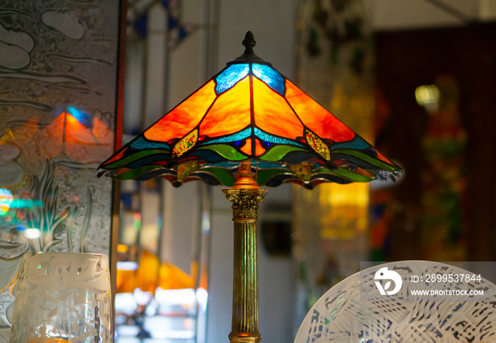 Multi color glass lamp . Interesting interior. Tiffany lamp on wooden table. Stained glass lamp, with a lampshade of colourful glass mosaic in green, yellow and red.