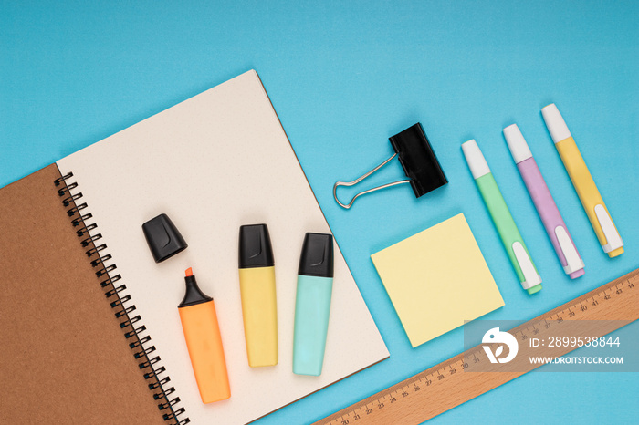 Notebook, colored pencils, ruler, note paper and clamp. back to school. Isolated blue background