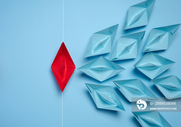 A group of blue paper boats and one red sailing against the current, concept of independent personality, breaking free from influence, strong leadership