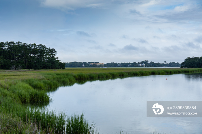 Sweeping waterway through a grassy salt marsh, treeline and early morning clouds and reflection, Mount Pleasant South Carolina, horizontal aspect