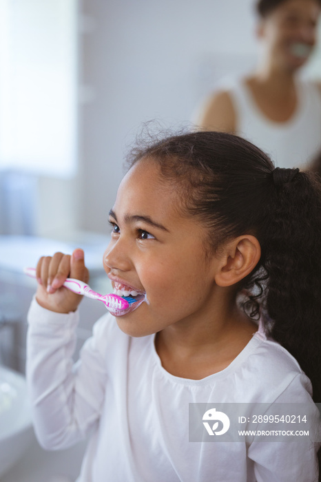 Multiracial girl brushing teeth while looking away with father in background