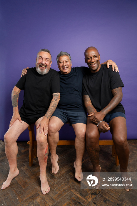 Portrait of two men laughing while sitting on bench against purple background