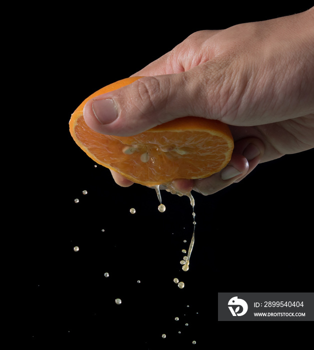 Hand squeeze orange slice with orange juice on black background