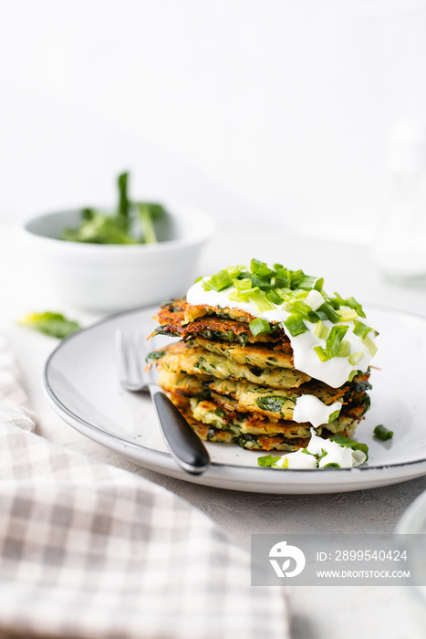 Potato pancakes with spinach, garlic and green onions served with sour cream dip on a plate on a light background