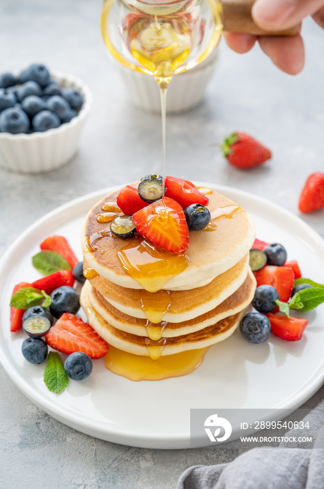 A stack of delicious fluffy pancakes with berries and honey on a white plate on a gray concrete background. Copy space.