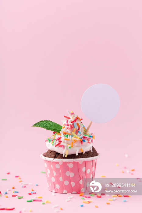 Sweet chocolate cupcake with empty white topper and sprinkles on pink background.