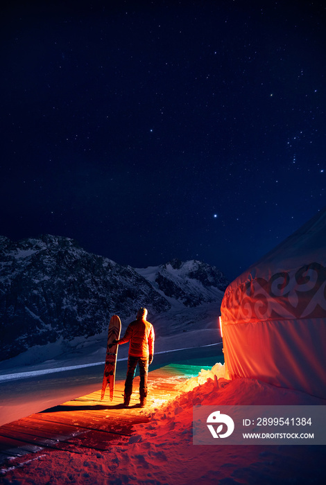 Man with snowboard near Yurt nomadic house at night at Mountains