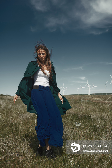 Woman with long tousled hair next to the wind turbine with the wind blowing