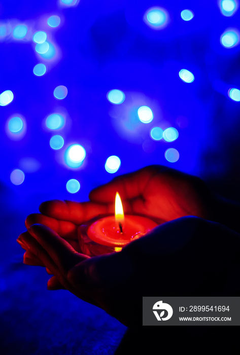 Burning candle in the hands of a girl with bokeh light. Christmas candles. Candlelight glowing in woman’s hands. Praying, faith, religion concept.