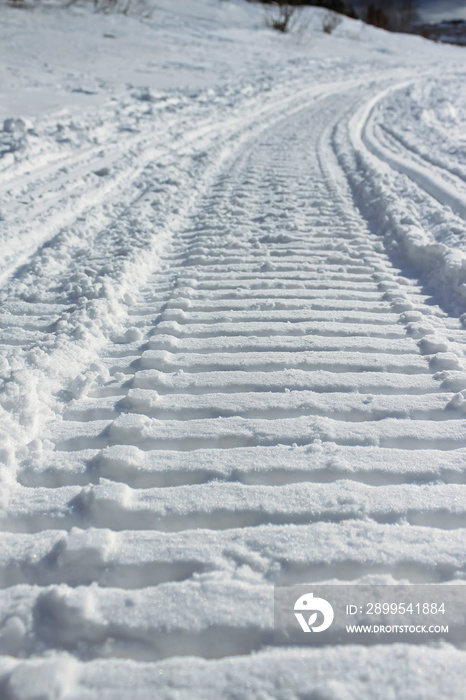 A close-up of a deep snowmobile track in the snow. The tracks go around the bend. Selective focus.