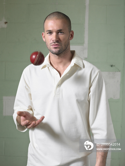 Portrait of a young cricket player with ball against green wall