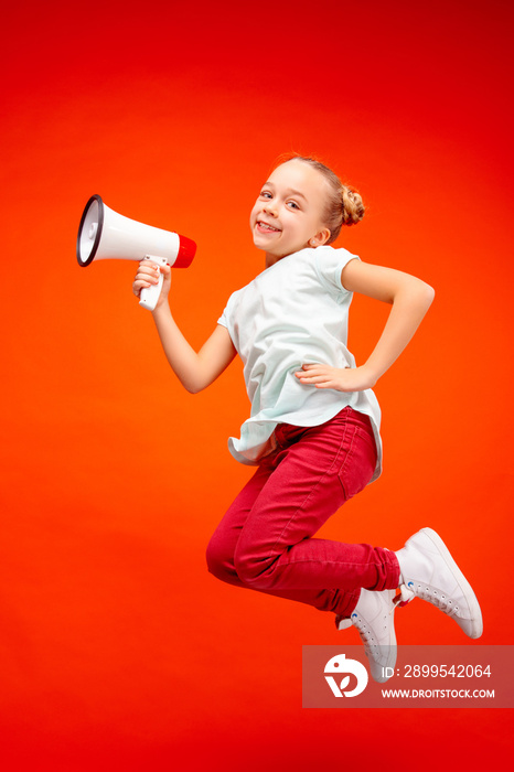 Beautiful young child teen girl jumping with megaphone isolated over red background. Runnin girl in motion or movement. Human emotions,, facial expressions and advertising concept