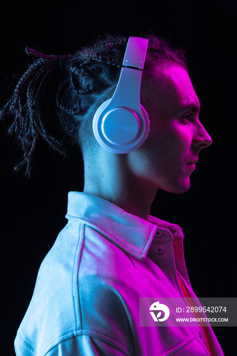 Close-up Caucasian young man isolated on dark studio background in neon. Side view